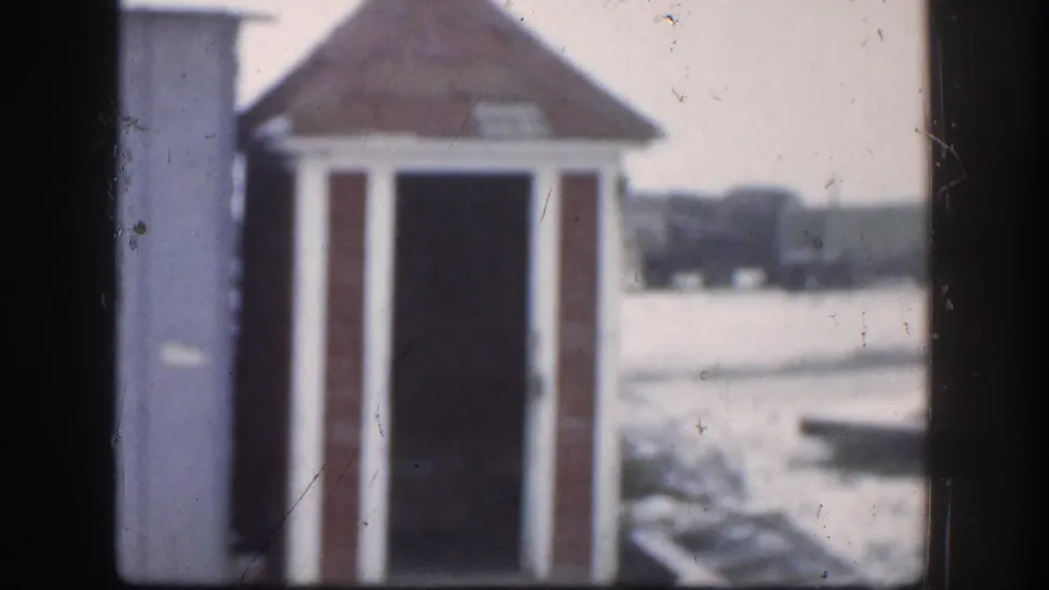 1958 Kansas home movie frame showing a small wooden outhouse with a red-shingled roof against a snowy rural landscape.