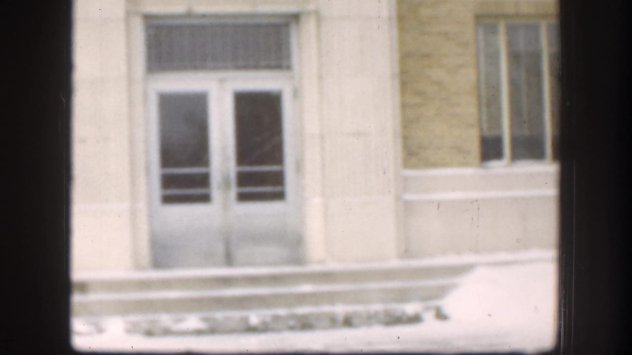 Entrance to a large institutional building, likely Kansas circa 1958, with double glass doors, stone columns, and snow resting on the exterior ledge.