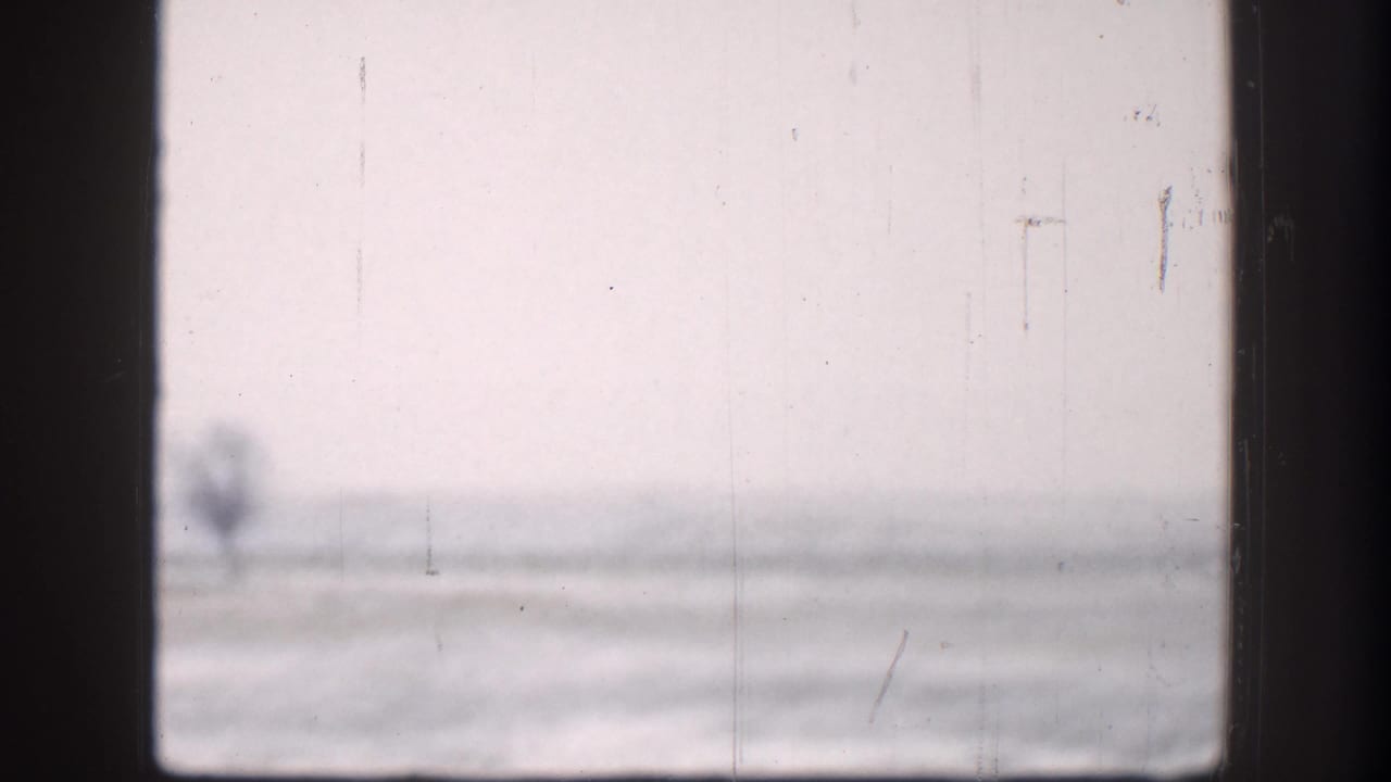 Washed-out 8mm view of flat plains through a window frame, Kansas circa 1958; overcast sky and faint horizon structure visible through heavy film grain.