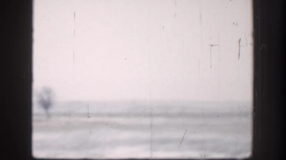 Washed-out 8mm view of flat plains through a window frame, Kansas circa 1958; overcast sky and faint horizon structure visible through heavy film grain.