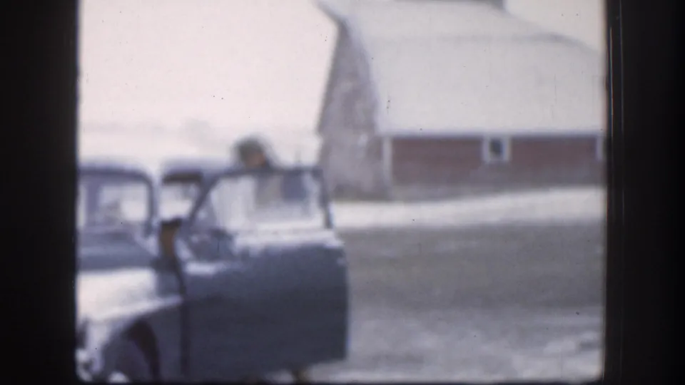 Adult loading an item into the open door of a large American sedan on a snowy rural Kansas farmstead, circa 1958, 8mm home movie.