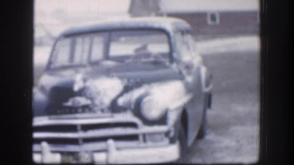 Front-on 8mm frame of a snow-covered 1950s American sedan on a Kansas farm, circa 1958; nearly identical framing to the preceding shot.