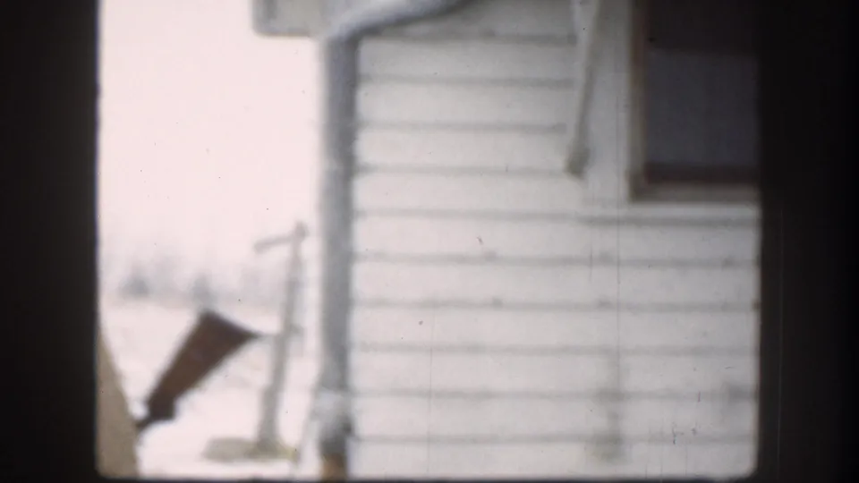 White clapboard house exterior with dark elongated prop object visible, 1958 8mm home movie, Kansas USA.