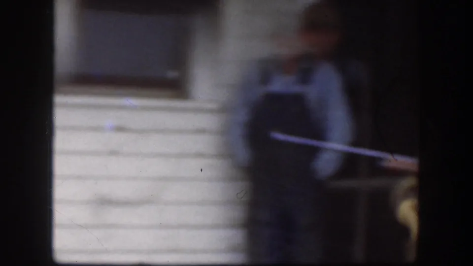 Motion-blurred frame with two figures near a white clapboard house exterior, from a 1958 8mm home movie, Kansas USA.
