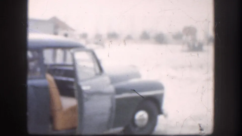 A late-1950s dark-blue station wagon with its rear door open stands in a snow-covered lot in what appears to be Kansas, 1958; the flat Great Plains horizon stretches behind it.