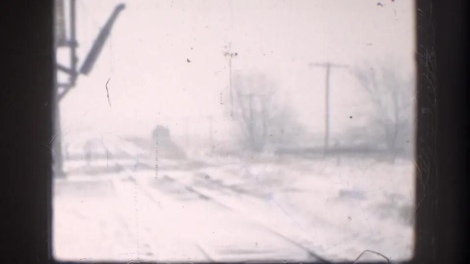 8mm view of a snow-blanketed Kansas landscape, circa 1958, showing railway tracks, utility poles, and bare trees nearly obscured by blizzard conditions.