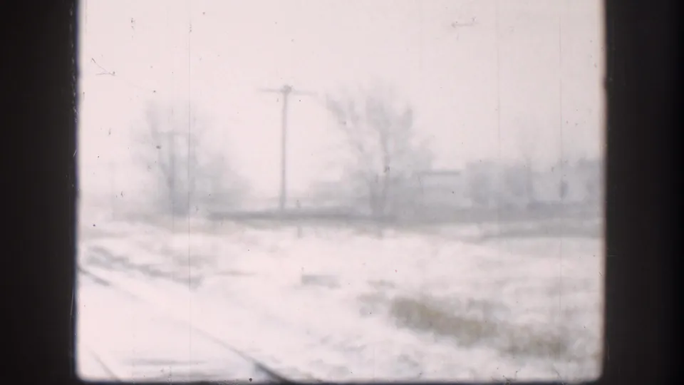 8mm footage of a Kansas railway corridor under blizzard conditions, circa 1958, with utility poles and winter trees at the edge of visibility.