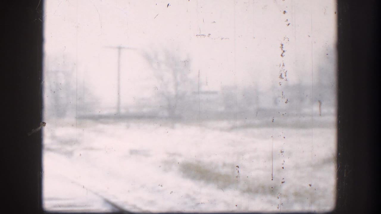 8mm home-movie view through a dirty window pane of a snow-covered Kansas railroad right-of-way during a 1958 winter storm.