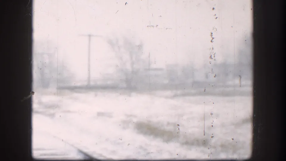Mid-20th-century 8mm footage of a snow-obscured Kansas landscape with railroad tracks, shot through a window during a winter storm.