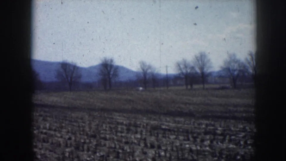 Wide landscape of plowed field with bare deciduous trees and what appear to be low rolling hills or a distant ridge, consistent with rural Nebraska circa 1958.