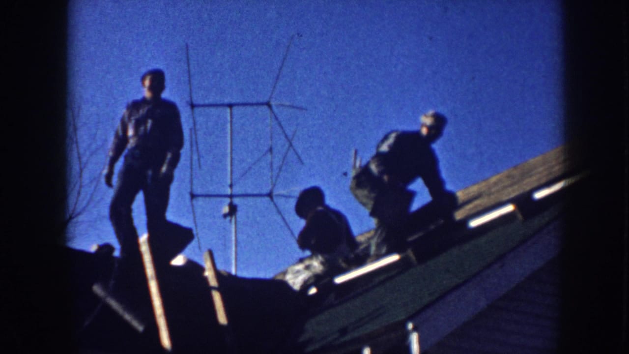 Three men working on a sloped shingle roof in Nebraska, c.1958, silhouetted against a vivid blue sky with a rooftop Yagi TV antenna behind them.