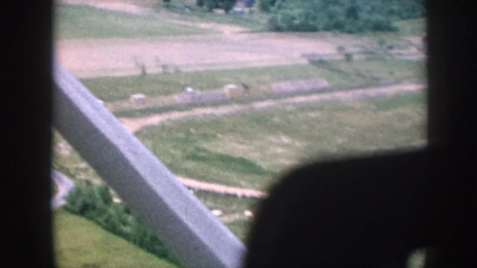 1958 8mm aerial view through light-aircraft struts over patchwork cultivated fields, a winding road, and small farm buildings, Nebraska.