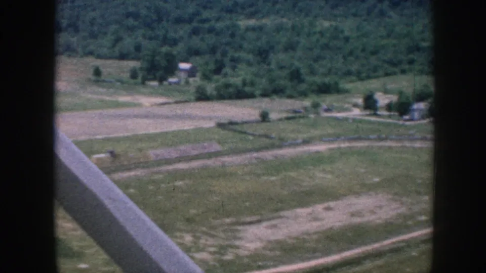 1958 8mm aerial view through light-aircraft struts over patchwork fields, scattered forest patches, and small rural structures, Nebraska.