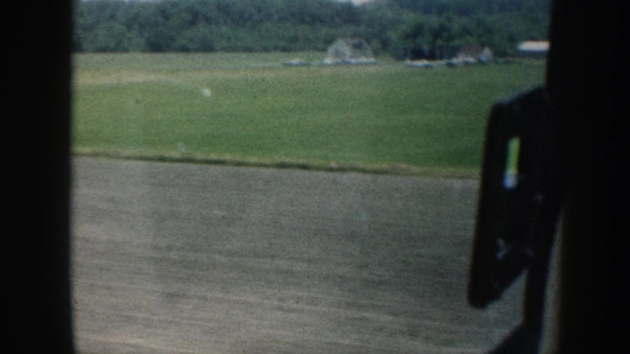Nebraska rural landscape circa 1958 framed by the car window; green pasture, a farmstead, and tree-covered hills visible as the vehicle moves.