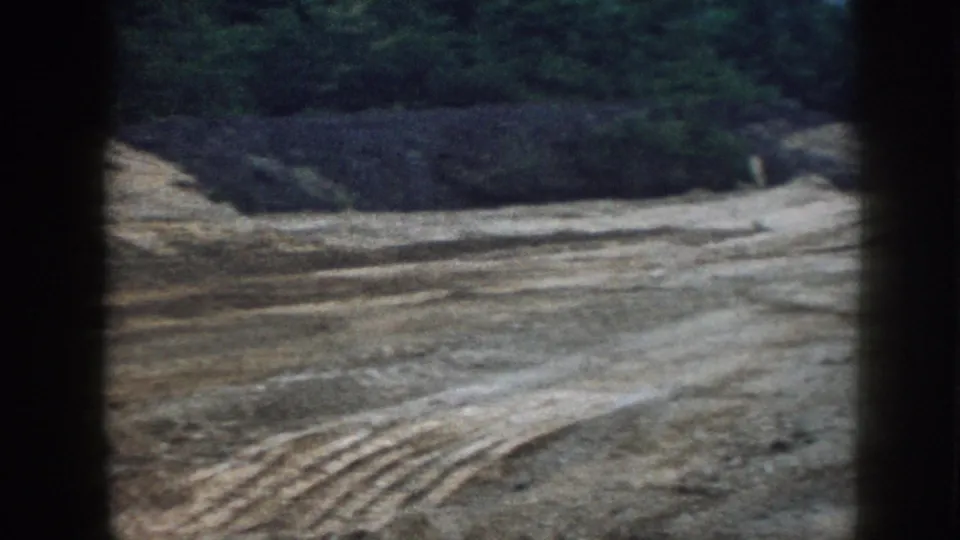 Freshly graded earth at a Nebraska construction site, circa 1958, showing blade tracks across leveled soil with mounds and deciduous trees in the background.
