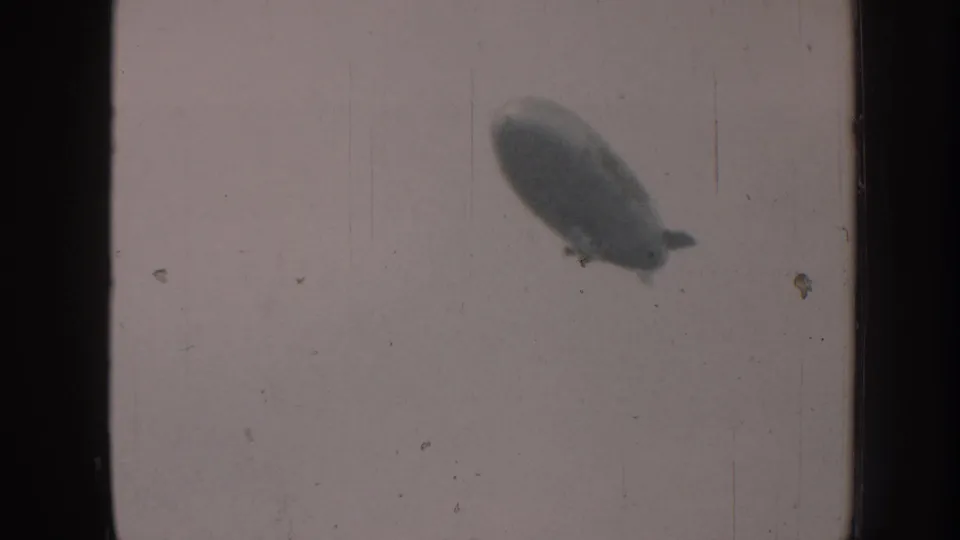 Clear blimp silhouette with gondola structure visible beneath the envelope, against a washed-out 8mm sky; consistent with a mid-century American airship overflight captured in 1958 Nebraska home movie footage.