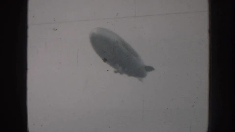 Airship with visible tail fins and gondola crossing overcast sky, 8mm home movie footage circa 1958, Nebraska USA.