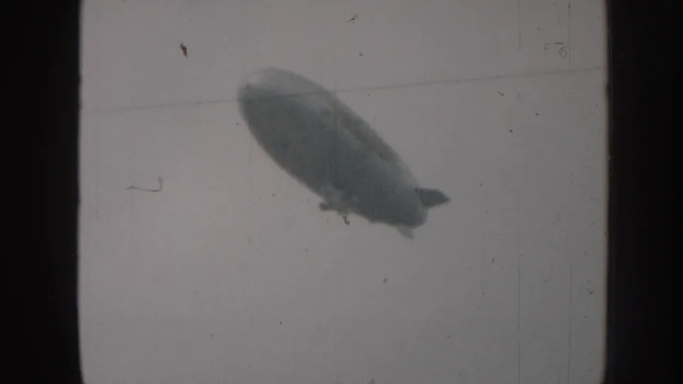 Airship passing above a diagonal power line in overcast sky, 8mm home movie footage circa 1958, Nebraska USA.