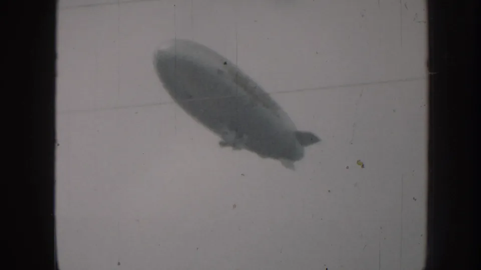 Cigar-shaped airship near the lower frame against overcast sky, 8mm home movie footage circa 1958, Nebraska USA.
