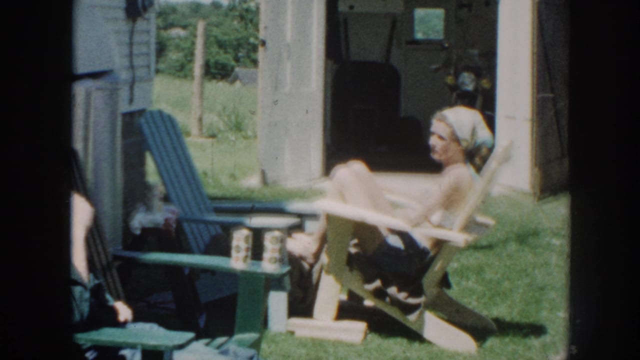 Woman in a light headscarf reclines in a wooden Adirondack chair outdoors, a small green table with cans visible to her left.