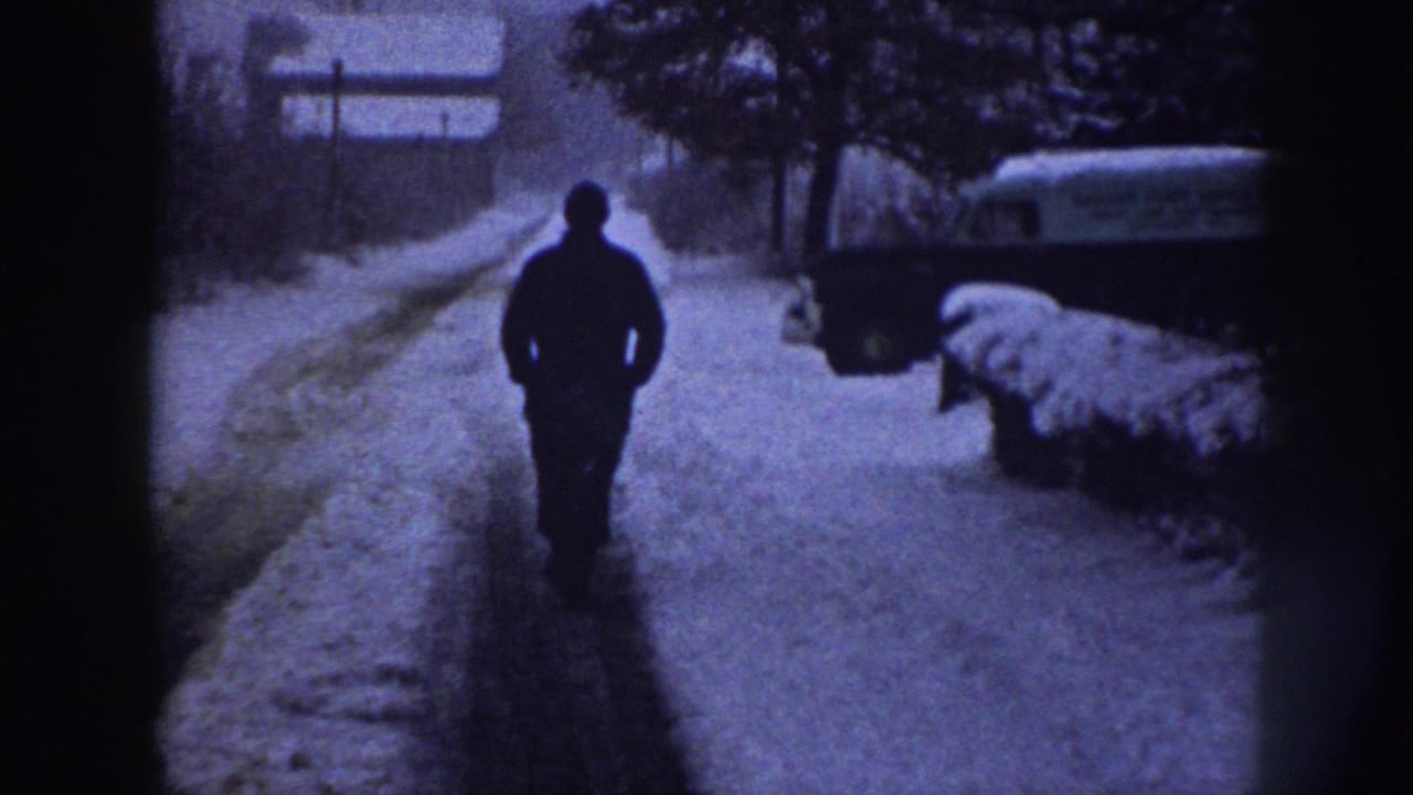 In Nebraska 1958 home-movie footage, a man walks down a snowy residential sidewalk with a parked vehicle nearby.
