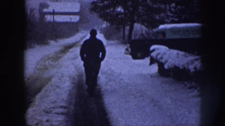 In Nebraska 1958 home-movie footage, a man walks down a snowy residential sidewalk with a parked vehicle nearby.