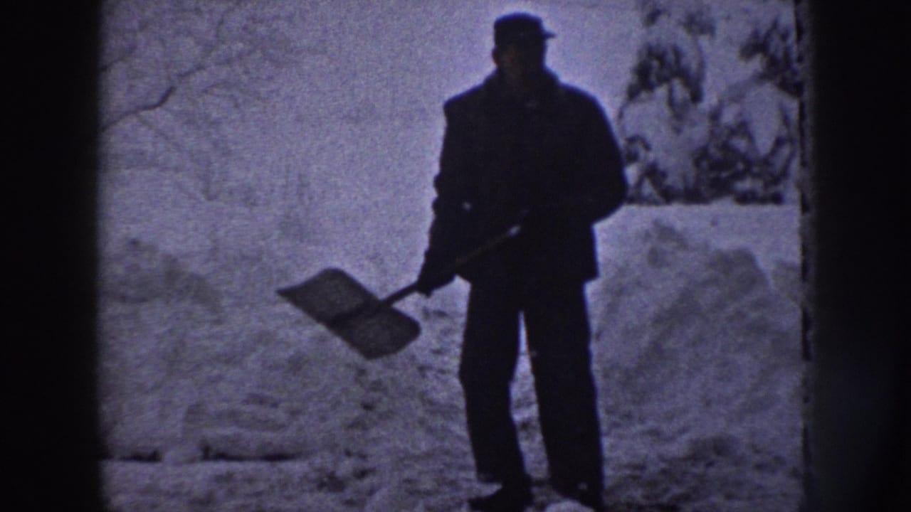 In 1958 Nebraska home-movie footage, a man stands in deep snow with a shovel near trees and a residential path.