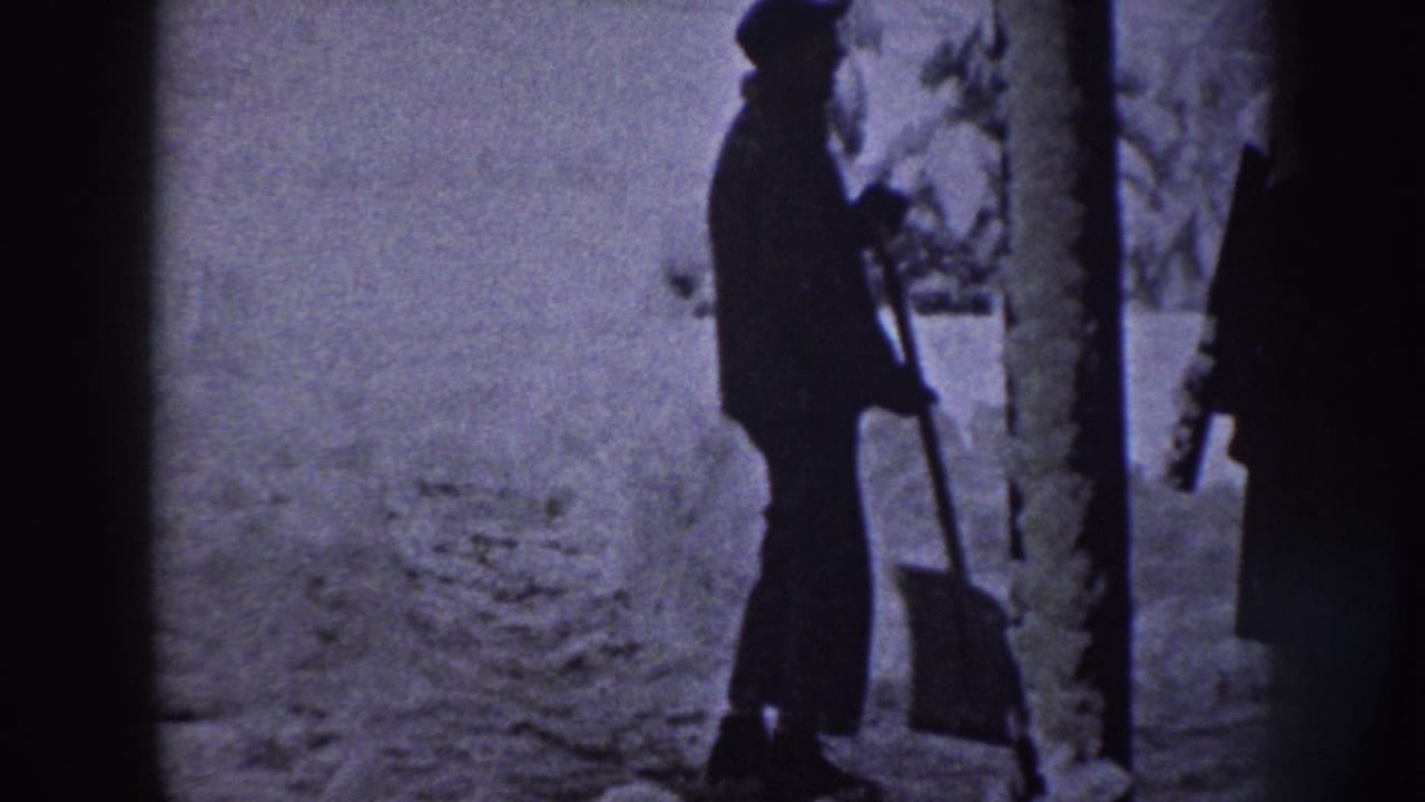 A man in winter clothing stands with a shovel in a snowy Nebraska residential yard, seen in soft 8mm silhouette.