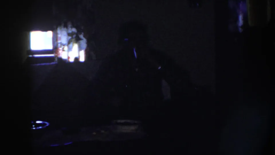 1958 Nebraska 8mm frame showing a heavily underexposed private room with a backlit opening and faint seated adult form.