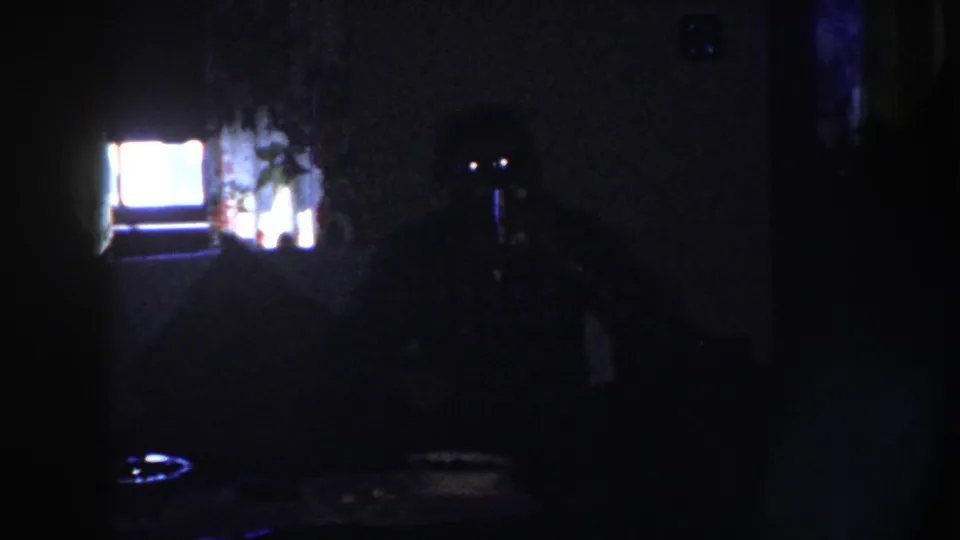 Dark 1958 Nebraska home-movie frame showing a dim room with a glowing television screen and indistinct household shapes.