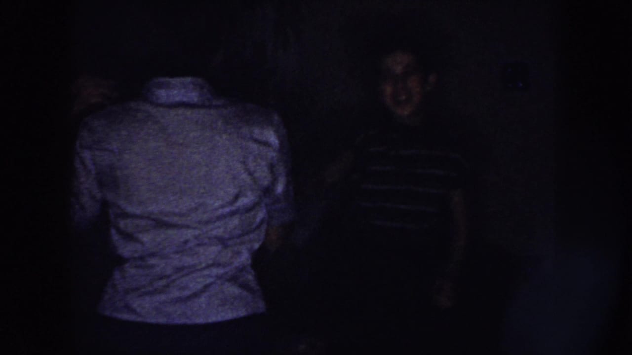 Two young women appear in a dim Nebraska home interior, one turned away while the other is partly visible in a striped shirt.