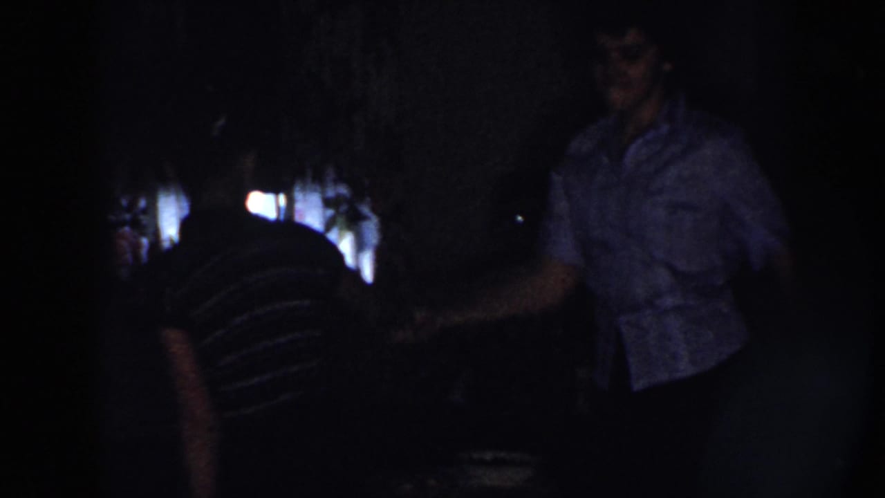 Woman in a patterned blouse dances beside a woman in a striped shirt in near darkness.