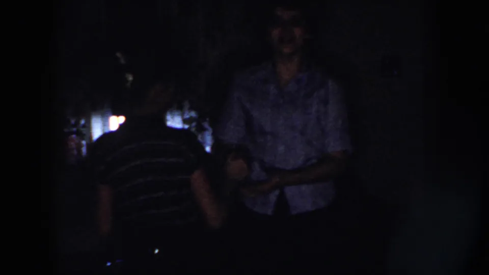 Two women appear close together in the dark 1958 Nebraska interior, with the patterned blouse figure more centered and screen light behind them.