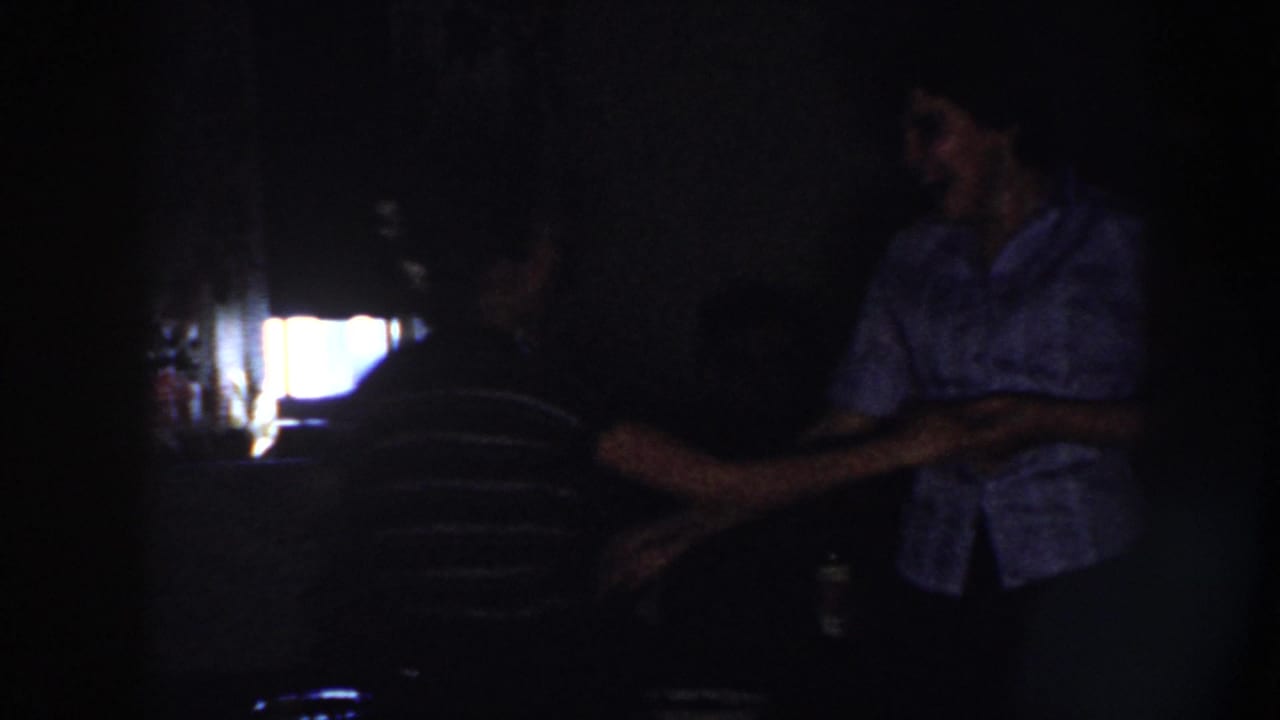 In 1958 Nebraska home-movie footage, a man in a light shirt and a woman in a dark striped top dance in deep shadow.