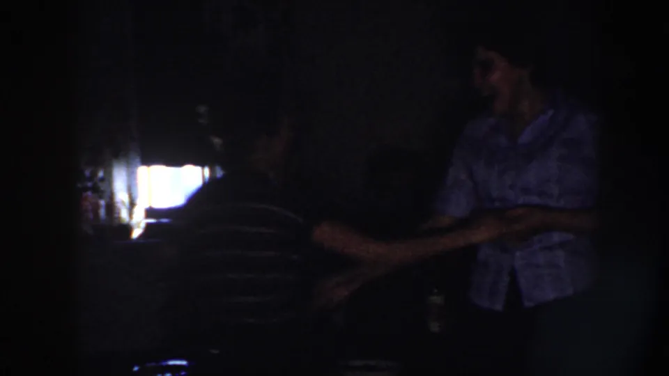 In 1958 Nebraska home-movie footage, a man in a light shirt and a woman in a dark striped top dance in deep shadow.
