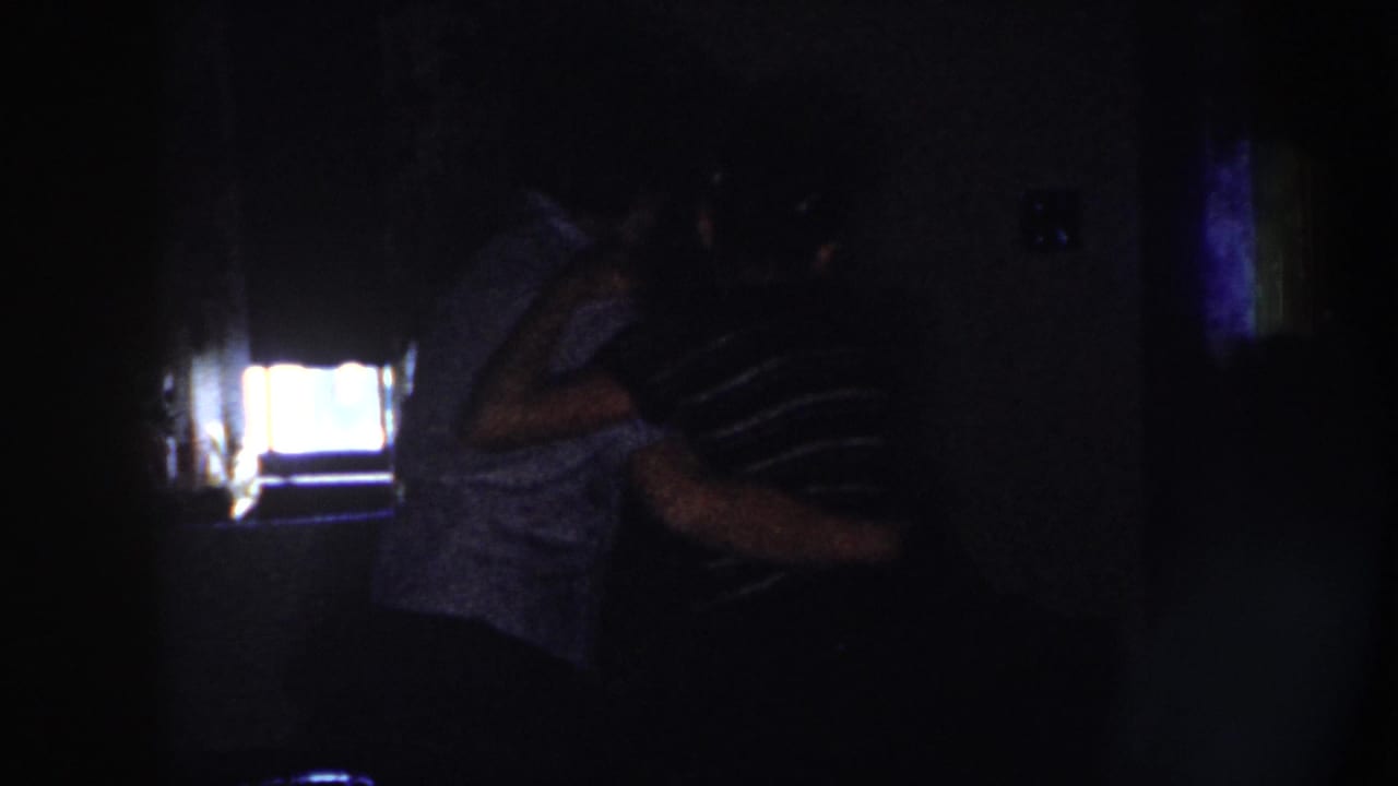 The dancing couple turns together in shadow beside a bright rectangular light.