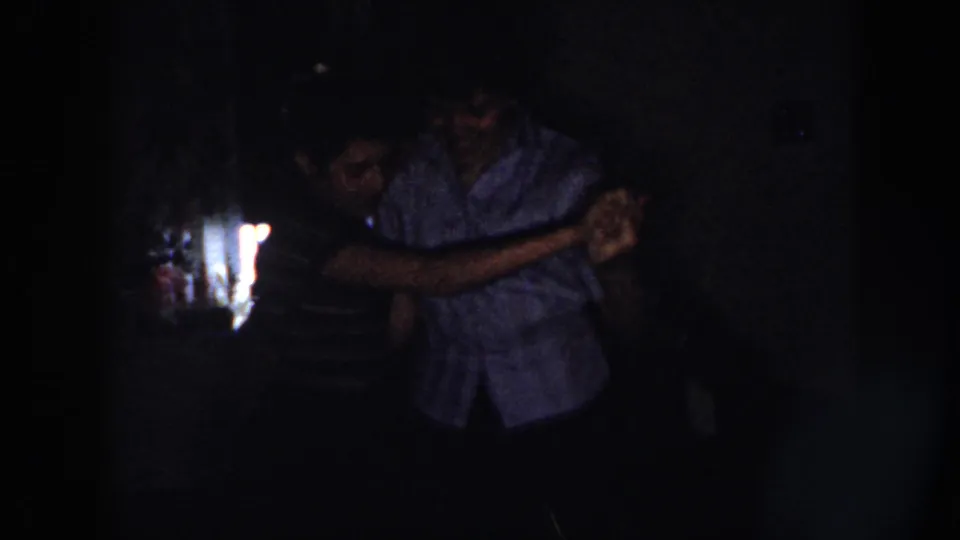A man and woman in 1958 Nebraska home-movie footage dance cheek-to-cheek or closely, with faces partly visible in low light.