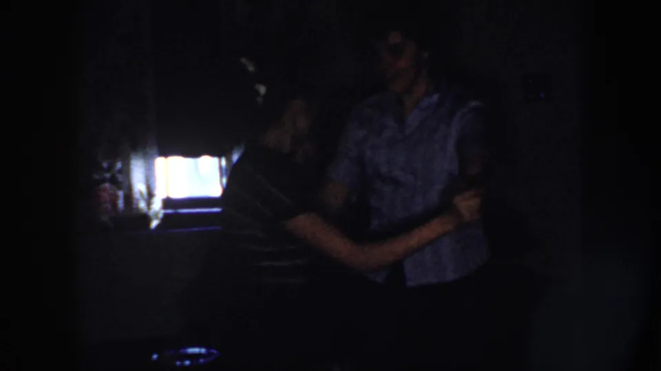 The adults keep dancing in the dark private interior, their clasped hands and bent posture visible against the bright background light.