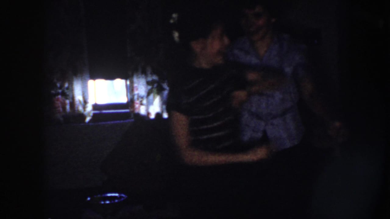 Nebraska 1958 home-movie frame showing two adults dancing in a dark interior, silhouetted by a bright window.