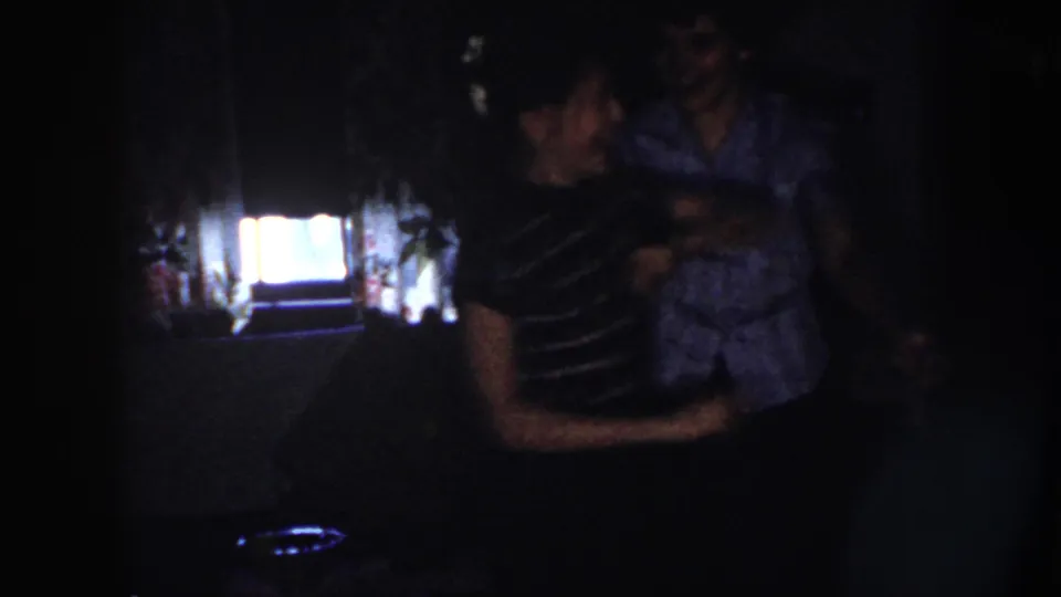 Nebraska 1958 home-movie frame showing two adults dancing in a dark interior, silhouetted by a bright window.