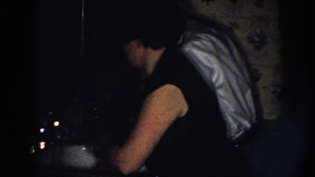 Woman with a light towel over her shoulder leans over a dark kitchen sink.