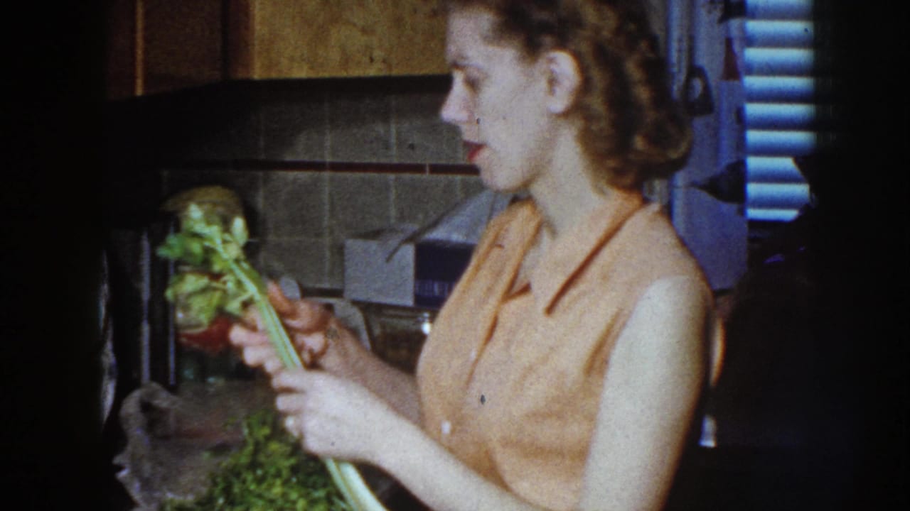 Adult woman in a 1958 Nebraska home kitchen holds celery beside a tiled backsplash and counter items.