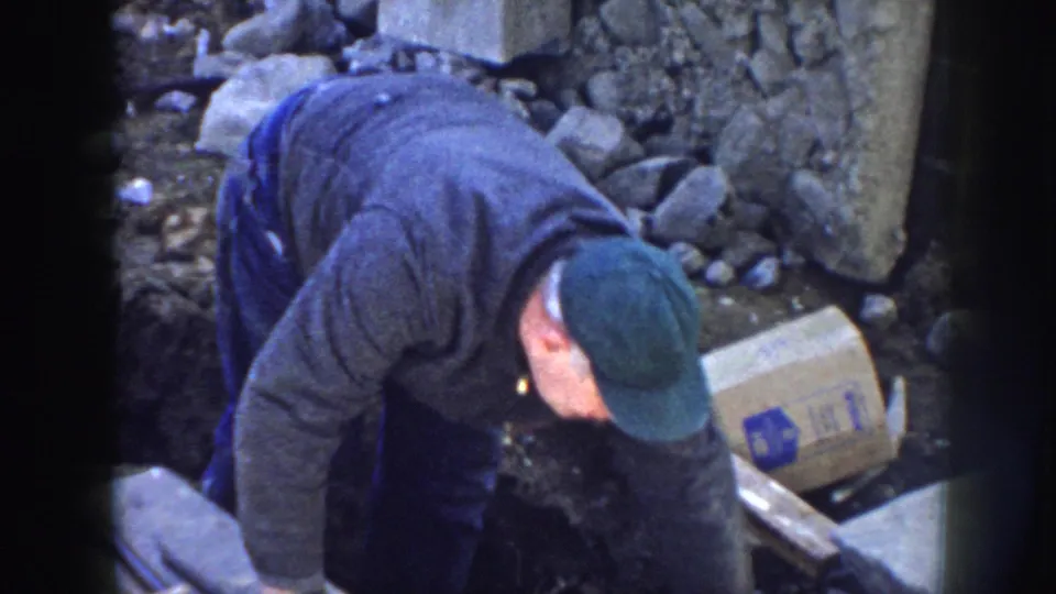 At the end of the 8mm clip, the Nebraska worker remains bent over the trench area amid lumber, stones, concrete, and a marked box.