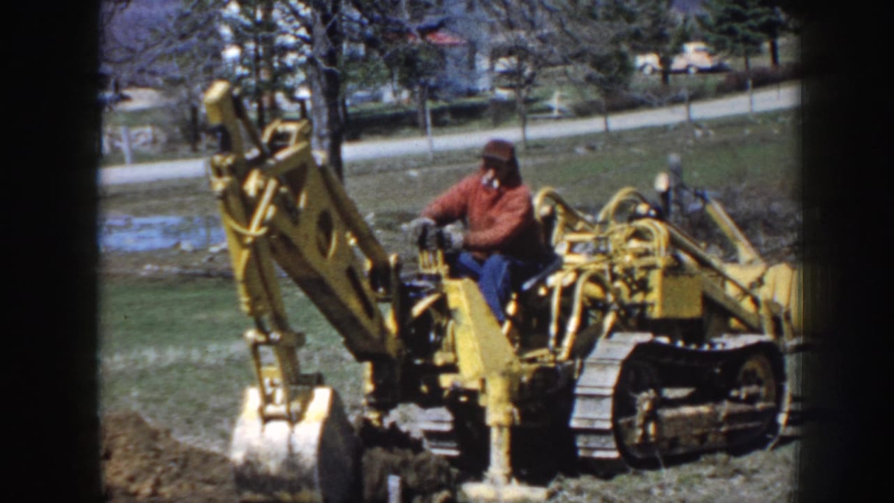 Tracked excavator digs into soil while the operator sits at the controls.