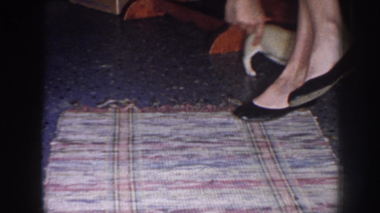 Woman's hand and black heels near a small puppy at the edge of a rug.