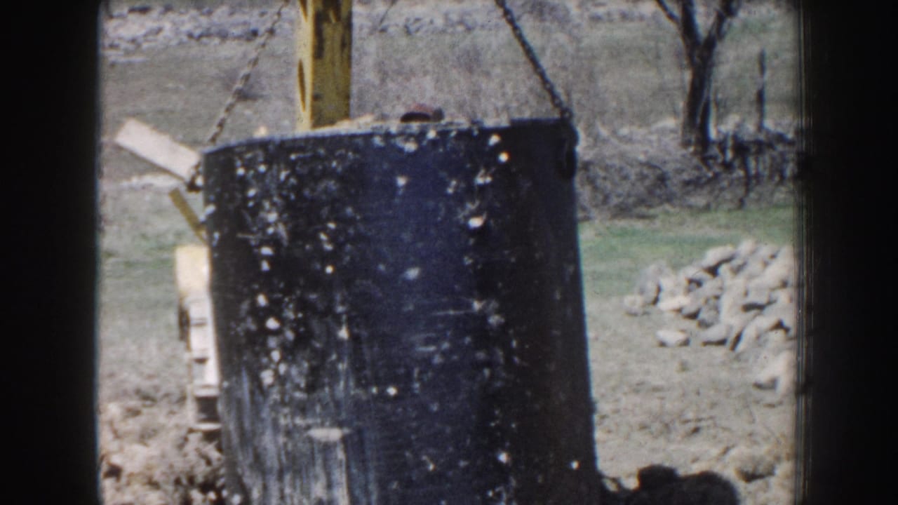 Black cylindrical septic tank beside a yellow excavator arm at a rural worksite.