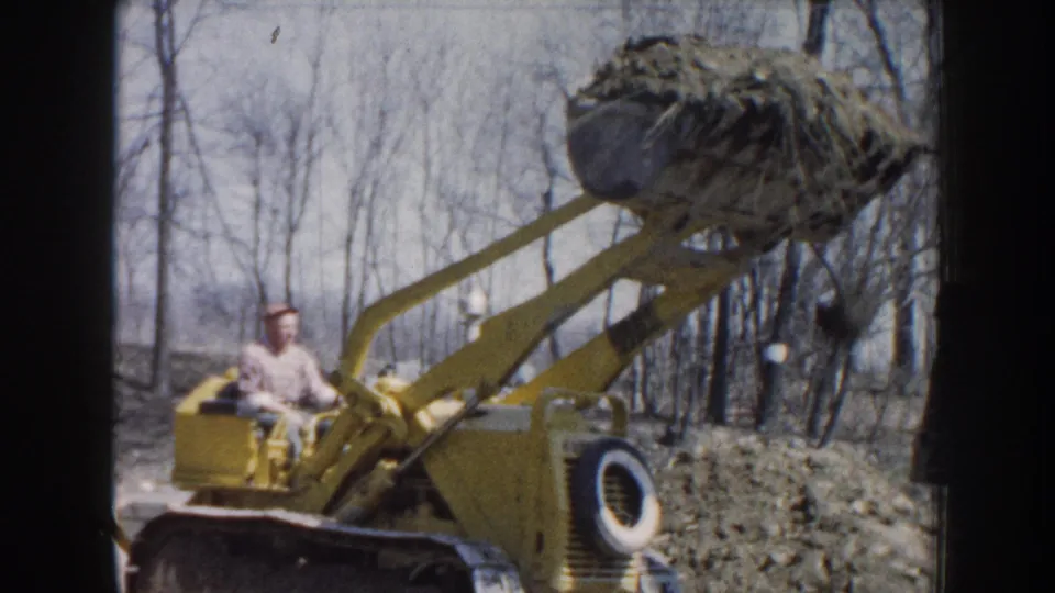 Side view of the 1959 Nebraska machinery scene, with the loader arms extended and the operator seated below the raised bucket.