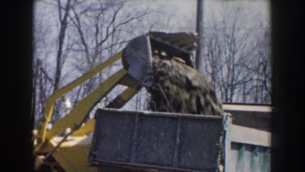 Raised loader bucket dumps loose dirt into a dark truck bed.