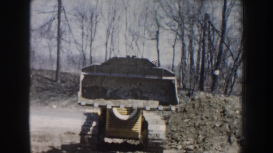 Rear view of a yellow tracked loader moving through a wooded Nebraska work area in 1959 home-movie footage.