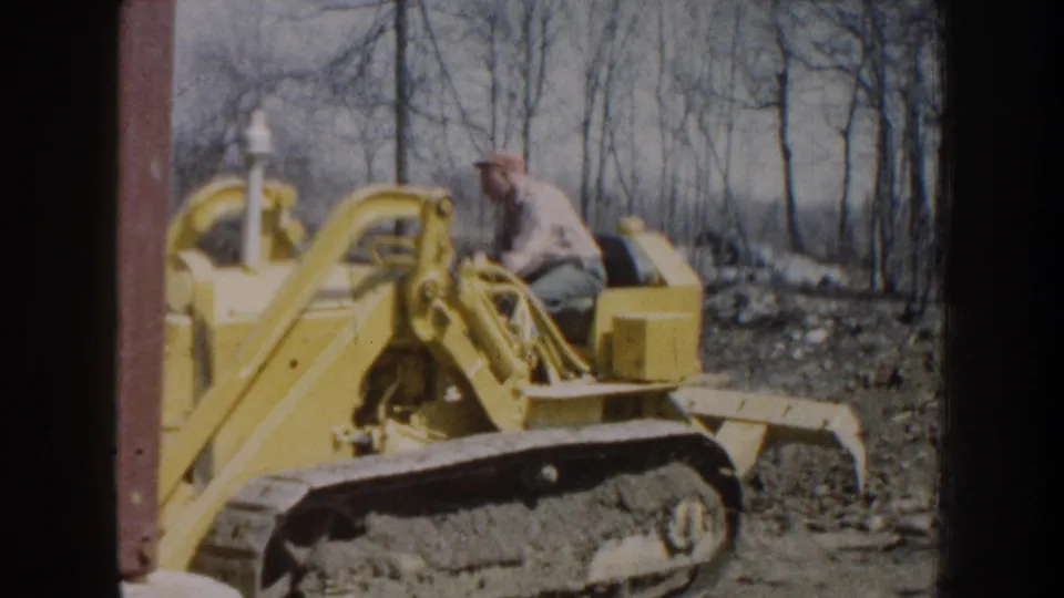 A 1959 Nebraska 8mm frame shows a man seated on a yellow tracked bulldozer, with dirt and leafless trees behind him.